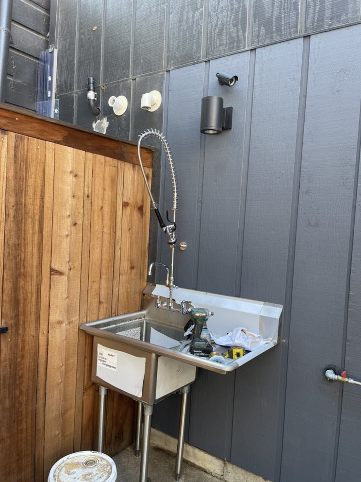 Commercial stainless steel utility sink with pre-rinse spray faucet installed at an exterior wash station